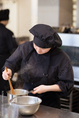 A chef in professional attire carefully stirs ingredients in a pot in a modern kitchen setting photo