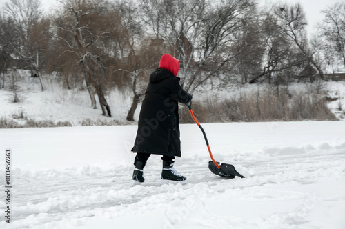 Snow removal with a shovel. A teenager clears a place from snow for skating. A boy with a black shovel removes fresh snow. Healthy lifestyle. Selective focus.