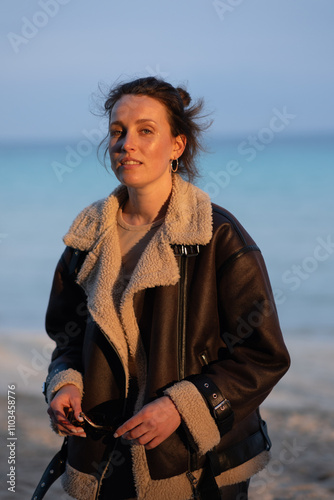 A beautiful girl in a sheepskin coat and sunglasses walks along the seashore in winter. Vacation in low season, a quiet walk by the sea, enjoying solitude, working with mental health alone