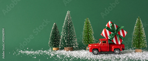 Photography A small red toy truck carrying a wrapped Christmas gift next to miniature snowy trees on a green background