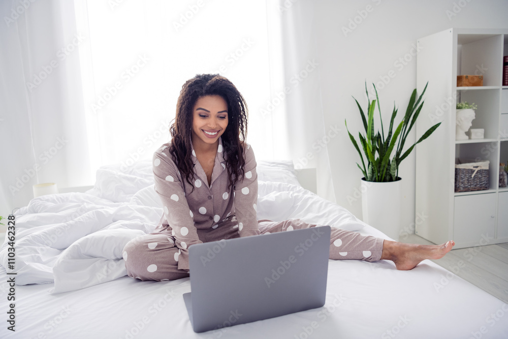 Young woman wearing polka dot pajamas enjoying leisure time with laptop in cozy bedroom Young woman wearing polka dot pajamas enjoying leisure time with laptop in cozy bedroom