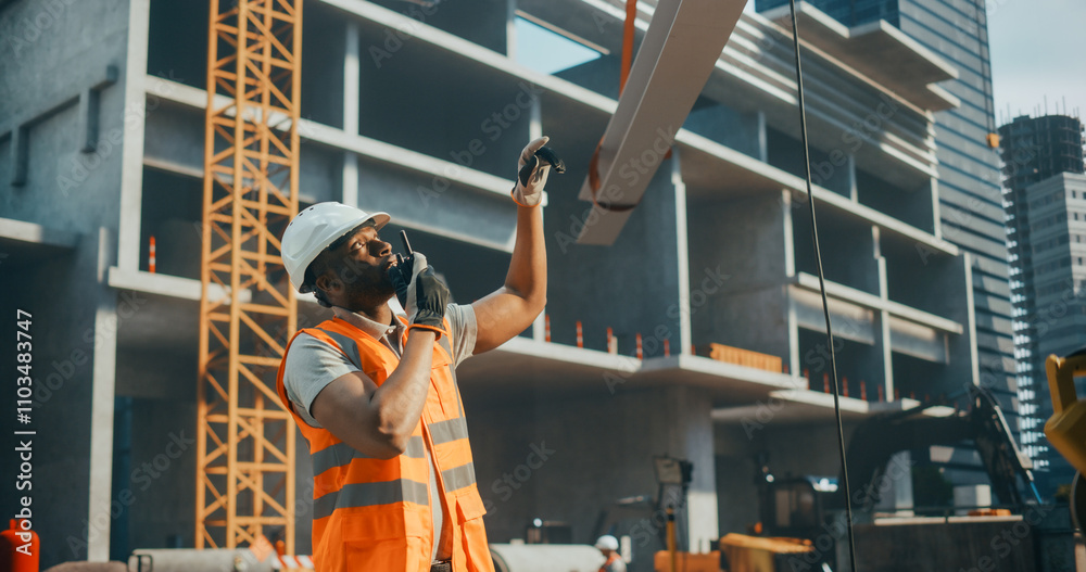Fototapeta premium Competent African American Contractor, Site Manager, Civil Engineer in a Hard Hat and Safety Vest. Black Man Helping a Crane Operator to Safely Move a Steel Beam at a Construction Site