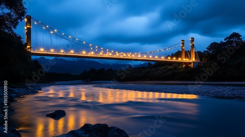 A modern suspension bridge illuminated by golden lights spanning across a river at night
