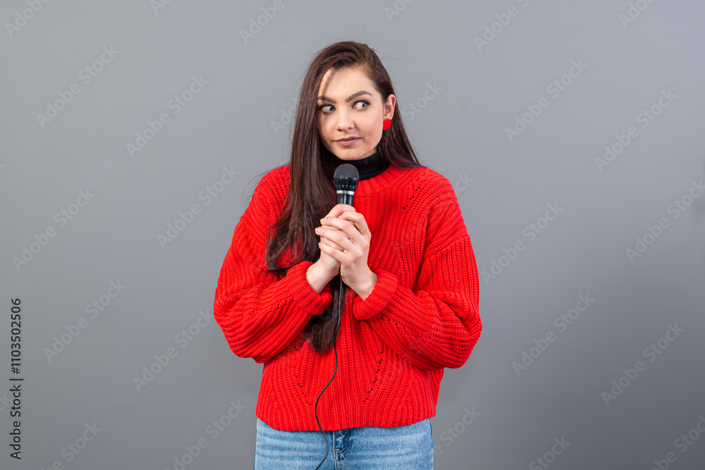 young, emotional brunette with a microphone dressed in a red sweater sings karaoke or says a speech young, emotional brunette with a microphone dressed in a red sweater sings karaoke or says a speech