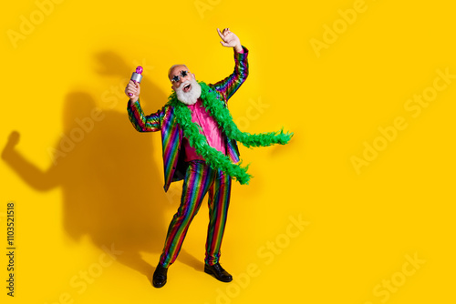 Full size photo of excited old man showman enjoy karaoke party wear glamour striped bright clothes boa sunglass isolated yellow background