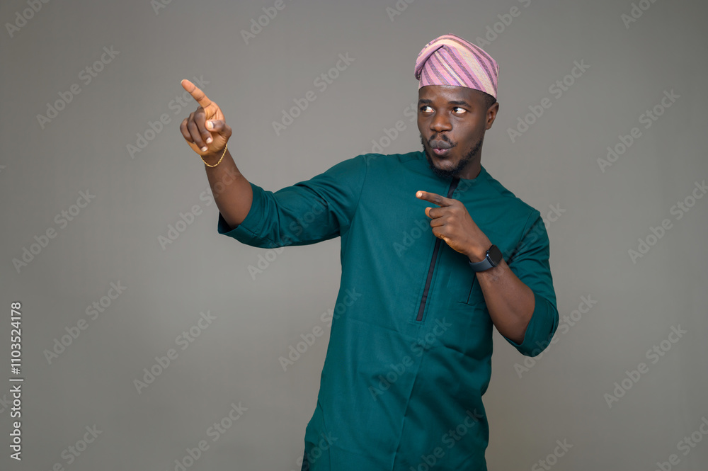 Young Handsome Nigerian Yoruba Man in Green Traditional Native Outfit and Matching Fila Cap, Smiling and Pointing with Both Hands at an Empty Space for Advertisement Placement Young Handsome Nigerian Yoruba Man in Green Traditional Native Outfit and Matching Fila Cap, Smiling and Pointing with Both Hands at an Empty Space for Advertisement Placement