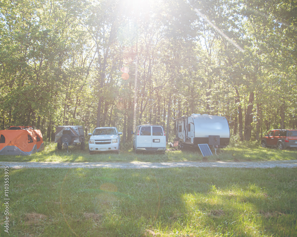Portable solar panel at country campground with row of RV trailer, camper, truck, tent setup in Mansfield, Missouri, lush green trees, gravel road, spring meadow campsite, nature outdoor living Portable solar panel at country campground with row of RV trailer, camper, truck, tent setup in Mansfield, Missouri, lush green trees, gravel road, spring meadow campsite, nature outdoor living