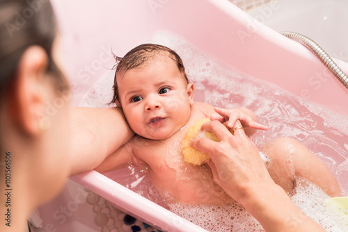 Mother cleaning 2 months baby in little bathtub at home