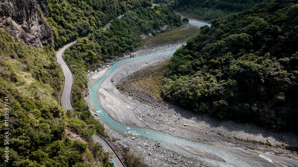 A winding road through lush mountains and a clear river in Taiwan during daylight hours A winding road through lush mountains and a clear river in Taiwan during daylight hours