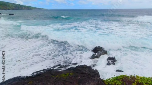 Maui's black sand beach with cyan water waves breaking on the shore, surrounded by lava rocks and sunny skies with light clouds at Wainapanapa Maui Hawaii photo