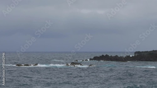 The scenic black sand beach near Hana, Maui, features crashing waves, rugged lava rocks, and sunny, lightly cloudy skies. Wainapanapa Maui Hawaii photo