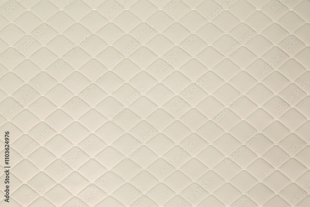 Fototapeta premium A close-up of a cream-colored automotive fabric with a diamond-shaped pattern. The fabric has a soft, luxurious, and vintage-inspired appearance.