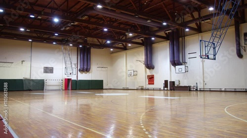 Empty basketball court in a gymnasium with a wooden floor and overhead lights