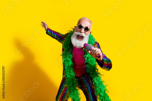 Photo of excited old man showman singing microphone wear glamour striped bright clothes boa sunglass isolated yellow color background