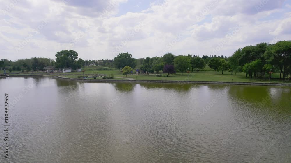 Calm waters reflect cloudy skies in a serene park setting with lush greenery and walking paths Calm waters reflect cloudy skies in a serene park setting with lush greenery and walking paths