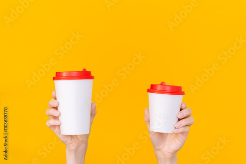 A woman's hand holding two white paper coffee cups of different sizes with a red lid. Copy space. Mock up. Isolated on an orange background. The concept of choice