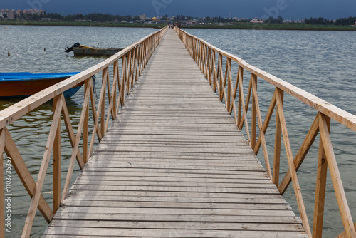 Wooden walkway leads to the Caspian Sea in Iran with boats and cityscape visible