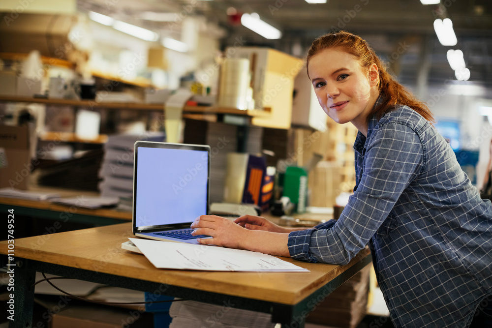 Young woman using a laptop while working in a printing press office