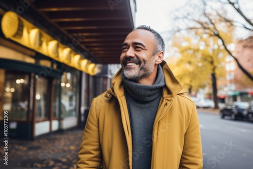 smiling middle aged man in yellow coat looking at camera in city