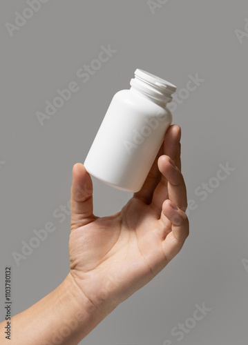 Female hand holding a white plastic pill bottle closeup against grey, Healthcare concept