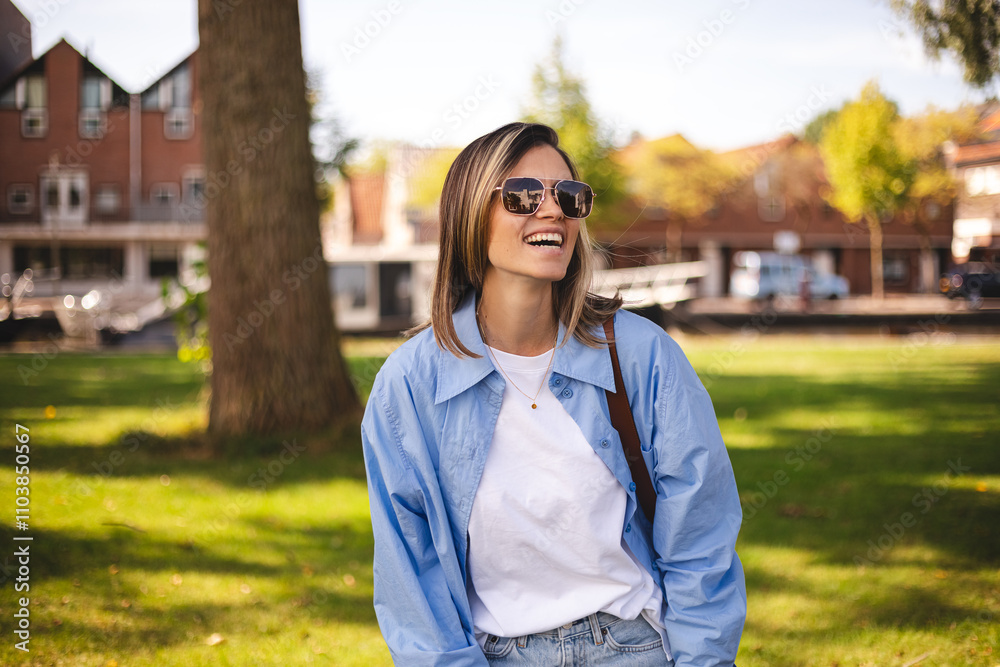 Beautiful woman in sunglasses, shirt, top smiling and look at camera in countryside. Outdoor portrait of a smiling blonde girl. Happy cheerful girl laughing at green city, look fashion. Beautiful woman in sunglasses, shirt, top smiling and look at camera in countryside. Outdoor portrait of a smiling blonde girl. Happy cheerful girl laughing at green city, look fashion.