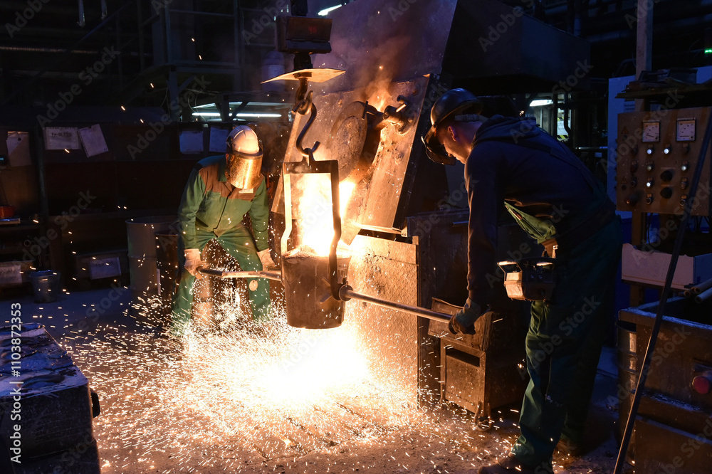Group of workers in safety clothing in an iron foundry - filling the casting ladle with hot metal - industrial production
