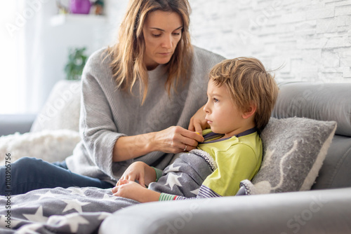 Sick child, preschool boy, lying in bed with a fever, resting at home with his pet dog, mom checking on him