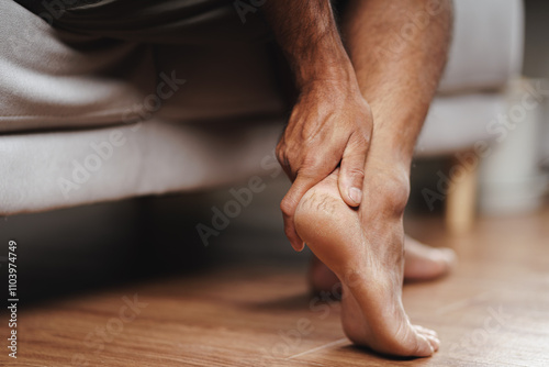 A man is sitting on a couch with his foot cracked hard skin on the heel. He has a foot blister and rubbing it