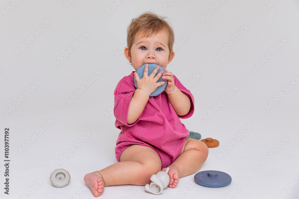 Happy smiling little baby girl, up to one year old, sits on the floor and plays with a multi-colored pyramid sorter on a white background. Development of fine motor skills. Early education. Copyspace Happy smiling little baby girl, up to one year old, sits on the floor and plays with a multi-colored pyramid sorter on a white background. Development of fine motor skills. Early education. Copyspace