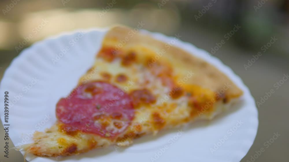 A hot slice of pepperoni pizza being held on a paper plate, with melted cheese and crisp edges, in a casual dining environment in 4K slow motion 120fps
