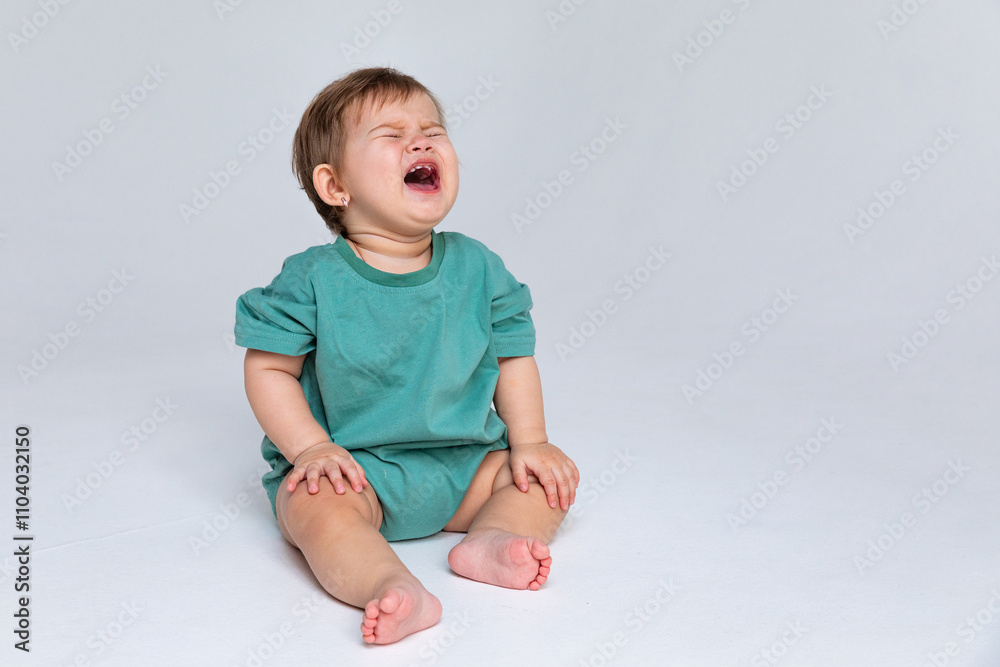 Little child baby in a green bodysuit sitting and crying isolated on a white background. Childhood concept. High quality photo. Copy space Little child baby in a green bodysuit sitting and crying isolated on a white background. Childhood concept. High quality photo. Copy space