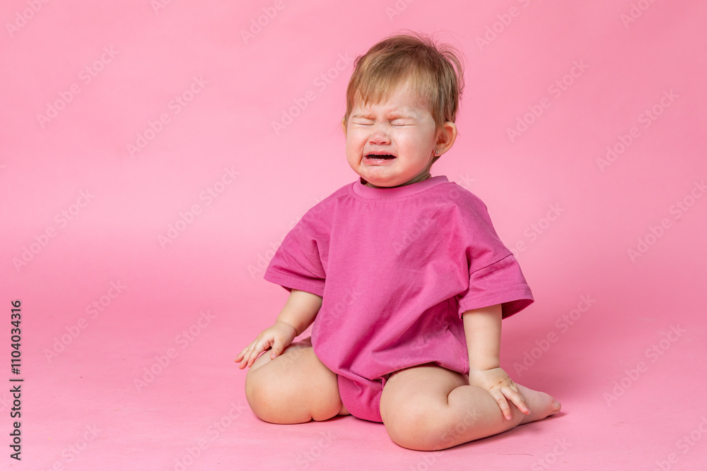 Little child baby in a pink bodysuit sitting and crying isolated on a pink background. Childhood concept. High quality photo. Copy space Little child baby in a pink bodysuit sitting and crying isolated on a pink background. Childhood concept. High quality photo. Copy space