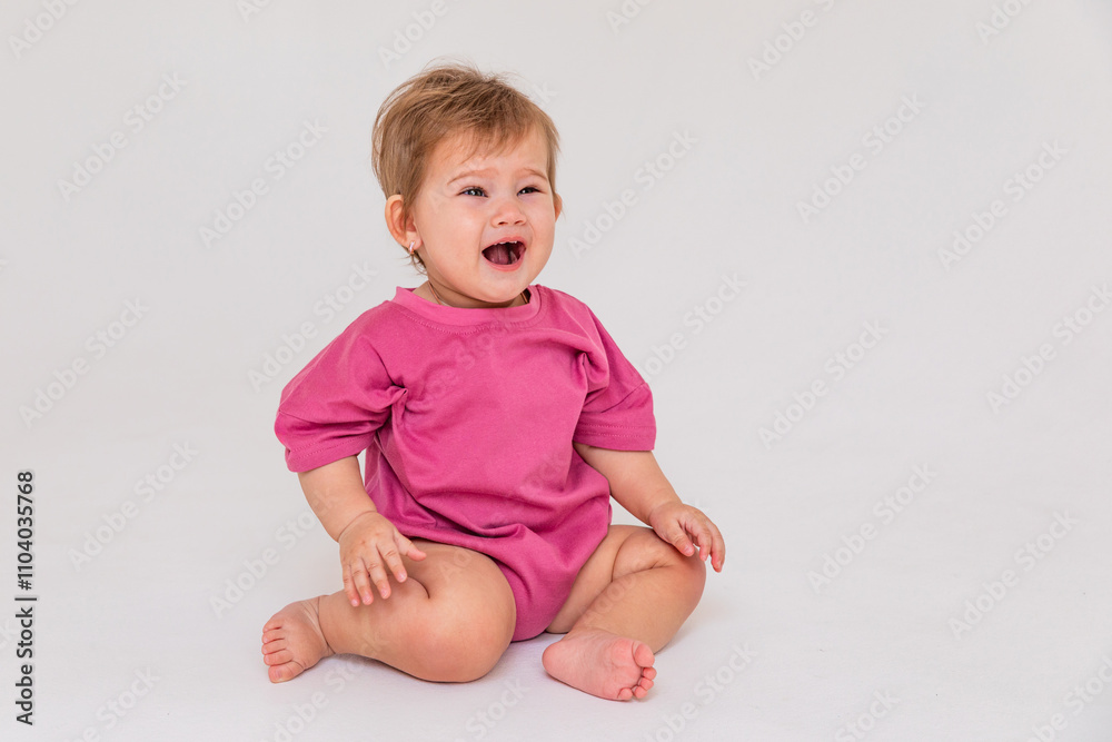 Little child baby in a pink bodysuit sitting and crying isolated on a white background. Childhood concept. High quality photo. Copy space Little child baby in a pink bodysuit sitting and crying isolated on a white background. Childhood concept. High quality photo. Copy space