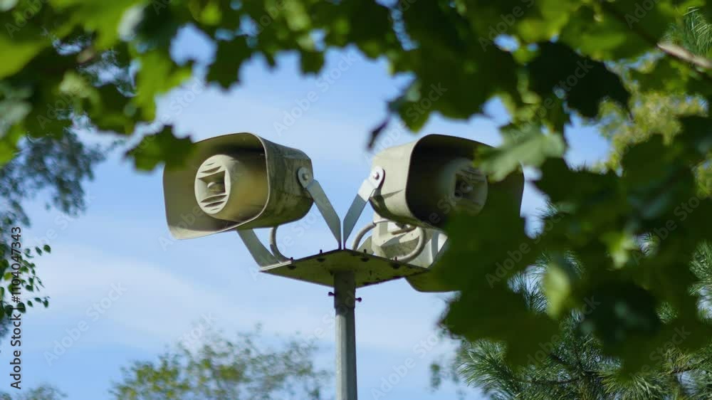 Outdoor warning siren speakers mounted on a tall pole, set against a bright blue sky and green foliage in 4K slow motion 120fps Outdoor warning siren speakers mounted on a tall pole, set against a bright blue sky and green foliage in 4K slow motion 120fps