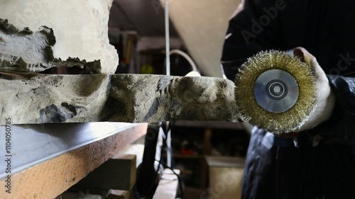 A worker uses a sander to process a cut of textured curved decorative wood in side view.  photo