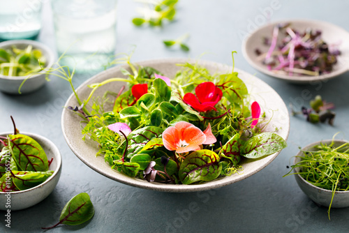 Green salad leaves with edible flowers in bowl. Grey background. Close up.