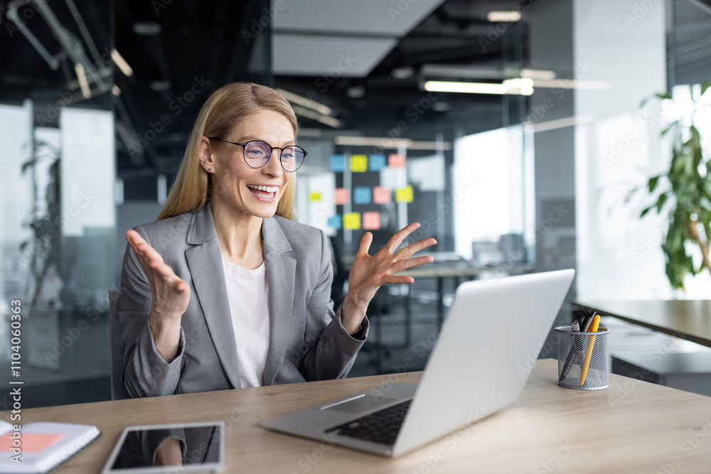 Mature woman businesswoman excitedly interacts during online meeting through laptop in modern office. Engaged in video call with enthusiasm, utilizing technology for remote work collaboration. Mature woman businesswoman excitedly interacts during online meeting through laptop in modern office. Engaged in video call with enthusiasm, utilizing technology for remote work collaboration.