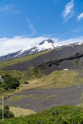 A stunning view of a volcano in a natural park in Chile during summer, surrounded by lush greenery and clear skies.