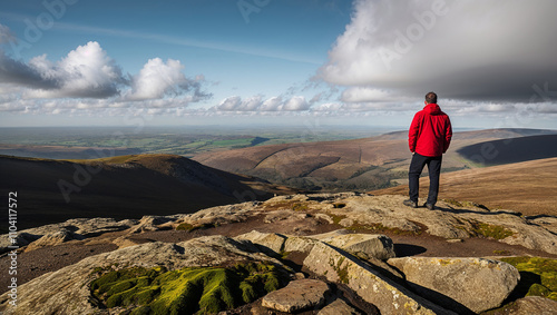 Individual views vast land from rocky peak beneath fluffy clouds.