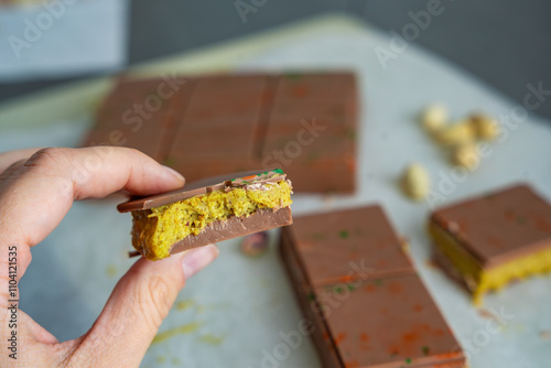 Piece of trend Dubai chocolate with pistachio paste and kataifi dough in woman hand. Confectionery handmade sweets at home in the kitchen.  photo