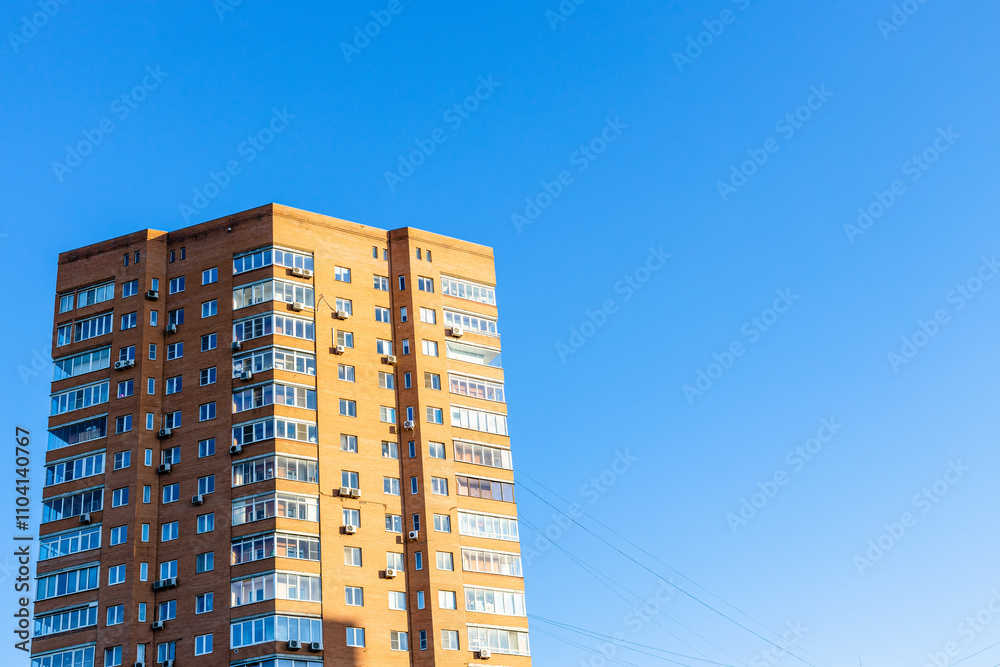 Fototapeta premium sunlit tower of brick high-rise apartment building