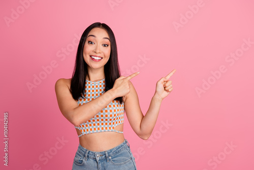 Joyful young woman in a trendy summer top pointing happily against a pink background, highlighting lifestyle and fashion