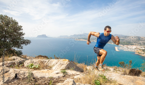 Man trail running on a rocky mountain path with ocean view photo