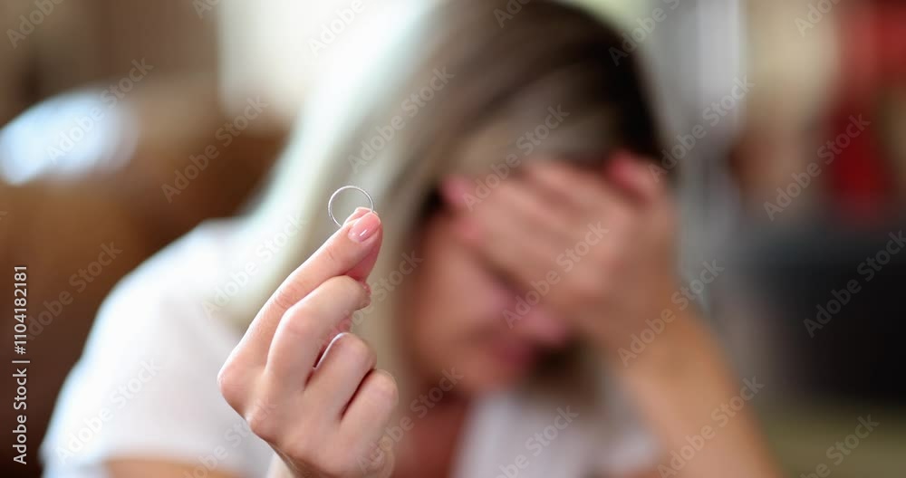 Distraught blonde woman makes facepalm gesture holding wedding ring. Frustrated lady goes through difficult divorce expressing negative emotions through tears
