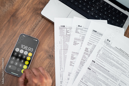 Person calculating taxes using a smartphone calculator with tax forms on a wooden desk. Financial management and tax filing concept. accountants, personal finance, and business tax preparation  photo