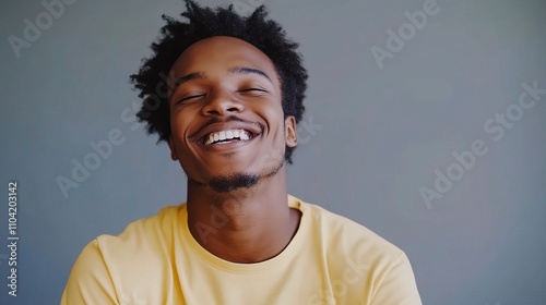 Smiling Young Man with Curly Hair in Yellow Shirt Against Wall