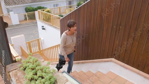 A Senior woman with pain expression suffers ascending stairs with crutch and knee brace for Stability and Safety, showing determination and resilience. Recovery rehabilitation. Horizontal footage 4k