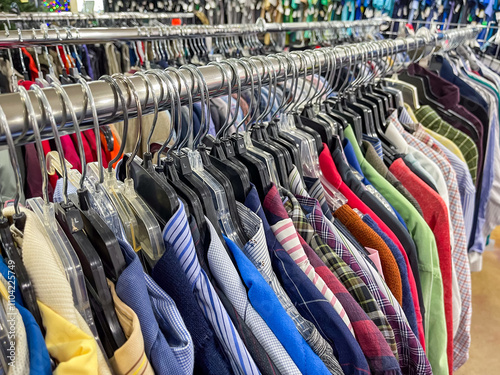 Thrift store clothing rack with selection of preowned secondhand shirts on hangers.