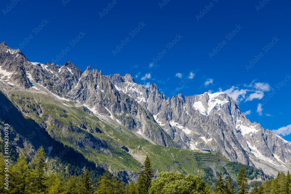Val Ferret mountain landscape in the Alps. Tour du Mont Blanc beautiful scenic view from the hiking path on the way from Itlay to Switzerland. Alpine meadow and high snow peaks of the Alps on the sun Val Ferret mountain landscape in the Alps. Tour du Mont Blanc beautiful scenic view from the hiking path on the way from Itlay to Switzerland. Alpine meadow and high snow peaks of the Alps on the sun