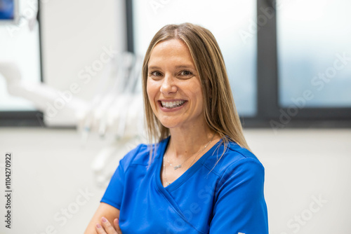 A smiling woman in a blue uniform sits confidently with arms crossed in a modern office setting, exuding professionalism and assurance in a calm environment. photo